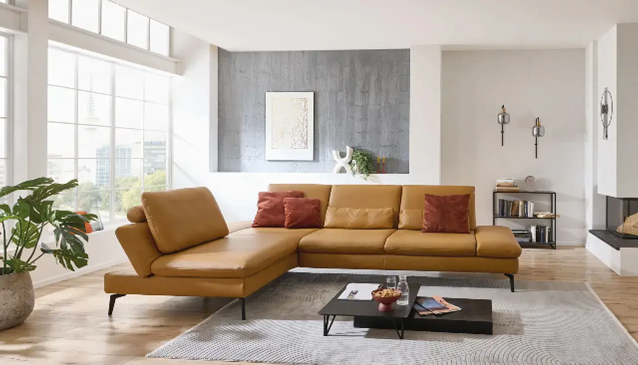 Stylisches gelbes Designer-Ecksofa mit roten Kissen in einem modernen Loft mit großer Fensterfront, grauer Wand und dekorativem Wandbild – elegantes Sofa für urbanes Wohnen.